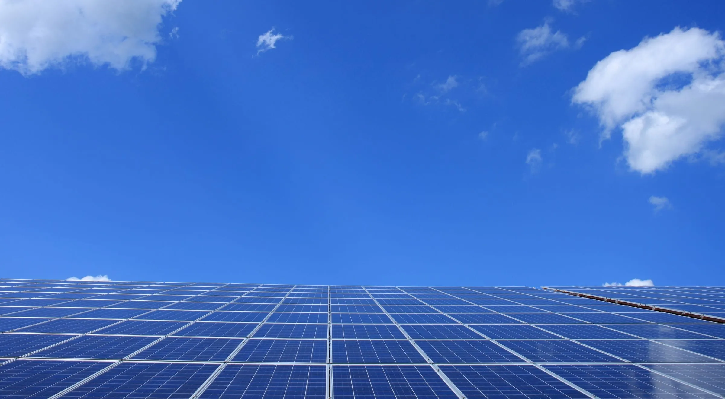 Rows of solar panels under a blue sky with scattered clouds