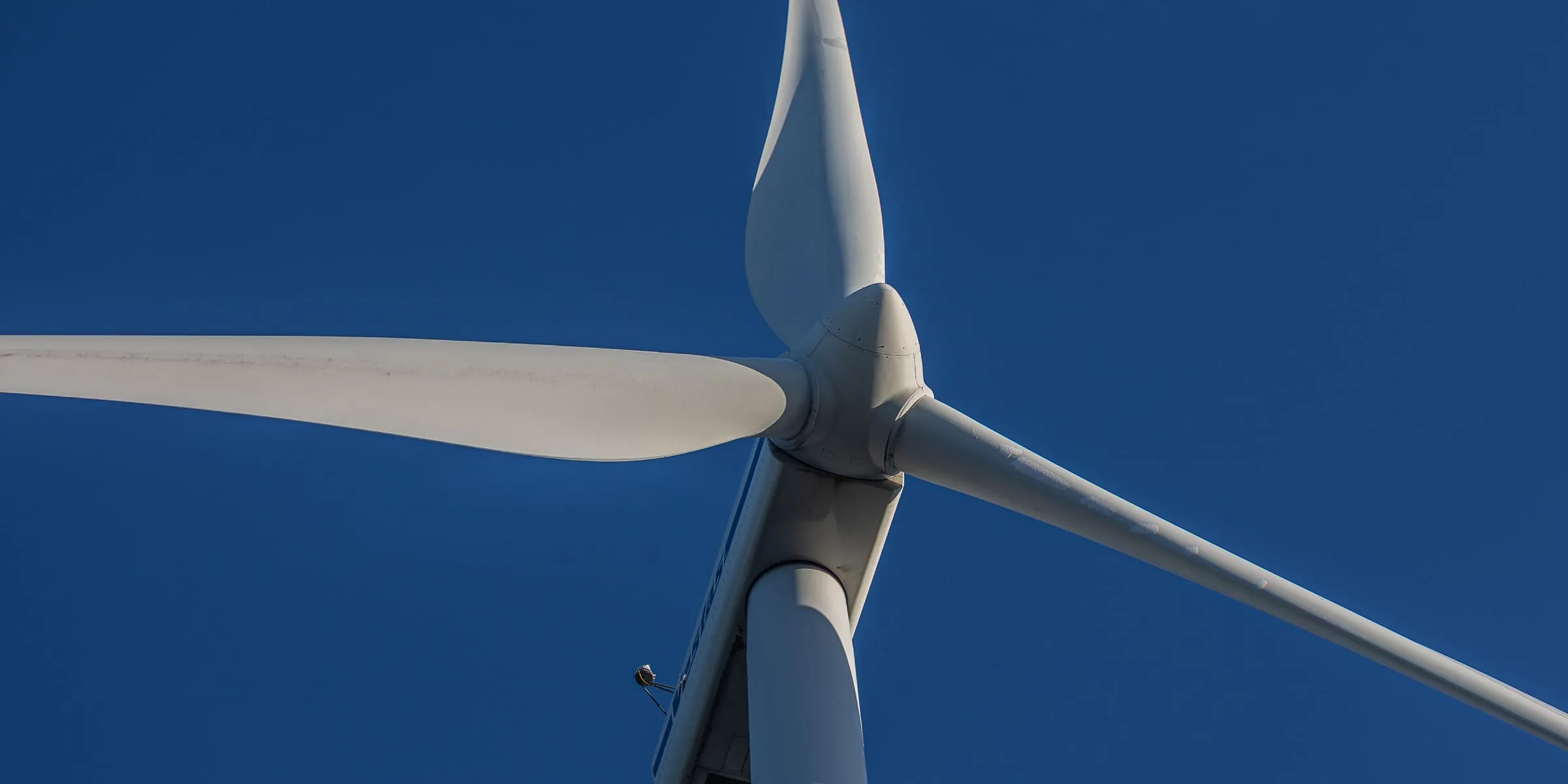 The hub and blades of a wind turbine against a deep blue sky